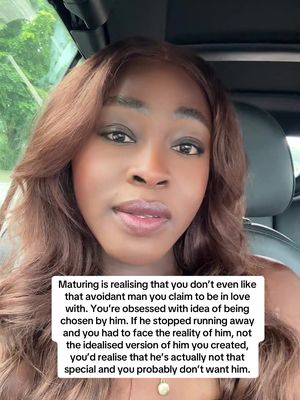 A selfie-style video featuring a dark-skinned woman with long, wavy brown hair. She is positioned inside a car, with the car's interior visible as a blurred background. The woman is looking directly at the camera with a neutral expression, and a text overlay is positioned near the bottom of the frame; the text appears in a white box with rounded edges.