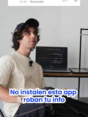 A young man wearing a black cap and a light beige t-shirt is looking towards the top left. Below his face is a white and blue rectangular text overlay that reads, "No instalen esta app roban tu info". Behind him is a white wall with a black laptop on the table. The whole shot is likely filmed indoors.