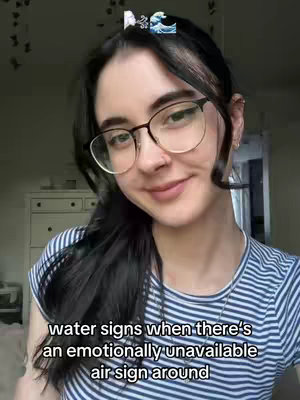 A selfie-style shot of a young woman wearing glasses and a striped shirt, set against a neutral background. She has dark hair, pulled back off her face, and is wearing a small decorative clip. Text overlayed at the bottom reads, 'water signs when there's an emotionally unavailable air sign around'.