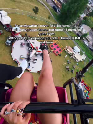 The cover image captures a first-person perspective from what appears to be a carnival ride. The viewer's legs, clad in shorts and with multiple rings on their fingers, extend down toward the ride's seat. The background includes the ride's mechanism, surrounding structures, and a grassy area with a few visible trees and buildings in the distance. Text overlays are added to the image with information.
