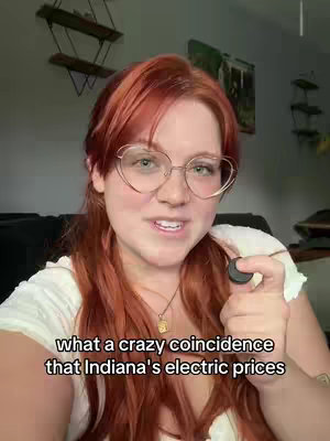 A woman with vibrant red hair and glasses is centered in a selfie-style video. She's holding a small round object, and a text overlay appears at the bottom.