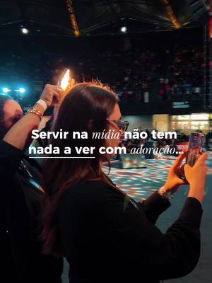A vertical shot showing a woman holding a phone in front of a brightly lit stage with many people. Text overlayed on the image reads in Portuguese.