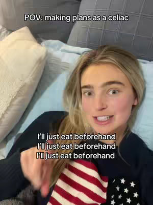 A young woman is lying on a bed with a light blue bedspread and pillows. The woman is wearing a dark sweater, and her facial expression is neutral as she is talking to the camera. There is text overlayed on the image.