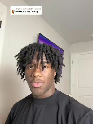 A young man with dark locs stands in front of a white wall and a television. His upper body and head fill most of the frame. He is wearing a black t-shirt and has a neutral expression with slightly pursed lips. Above him, a comment bubble contains the hook text.