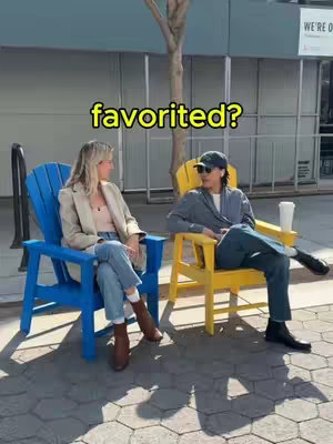 Two people are seated in oversized chairs on a patio. One is in a blue chair, the other is in a yellow chair. Text that says "favorited?" appears in yellow across the top of the image.