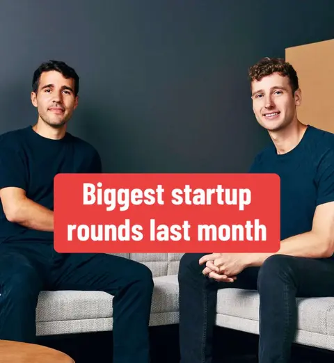 Two men are seated on a gray couch against a dark teal wall. A red rectangle with white text overlays the image, which is a close-up composition.