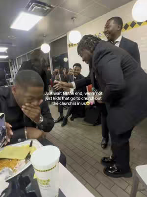 An interior shot inside a Waffle House, featuring a group of people in suits. One man is covering his face while seated at a table with a plate of food and a drink, while others in suits are standing around, some laughing or reaching out as if in a greeting or interaction. Overlaid text provides context to the scene.