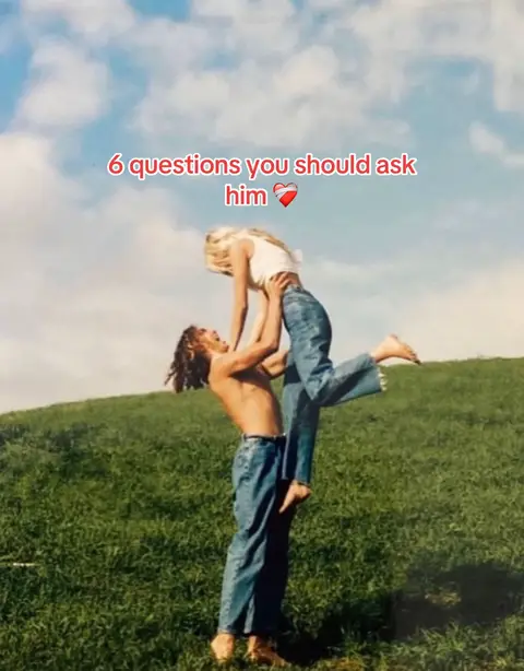 A vintage-style photograph shows a man holding a woman overhead against a backdrop of a grassy hill and a partly cloudy sky. The woman's arms are raised above her, and they are both wearing casual clothing. Overlayed text in red reads, '6 questions you should ask him with a heart emoji.'