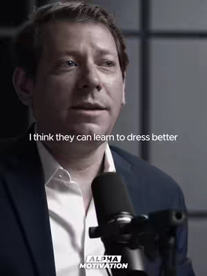 A medium shot of a man wearing a suit jacket speaks into a microphone. The background is a plain gray. The text overlay reads "I think they can learn to dress better". At the bottom left corner is the Alpha Motivation logo.