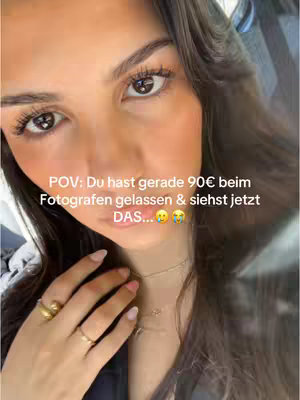 A close-up shot of a woman's face. She has dark hair, fair skin, and is wearing rings and a necklace. The background is out of focus.