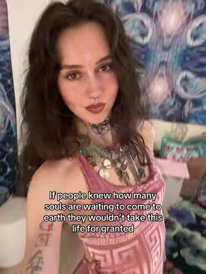 A woman with long dark hair, a nose ring, and a necklace stands, facing the camera. Behind her, a patterned wall provides a colorful backdrop. Text overlayed in a corner states, "If people knew how many souls are waiting to come to earth they wouldn't take this life for granted."