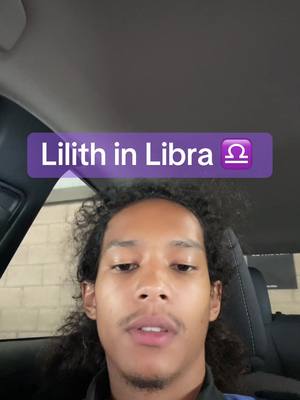 A selfie-style shot of a man sitting in a vehicle. The man, of African descent, has curly dark hair and a trimmed mustache and goatee. He gazes at the camera with a neutral expression. A purple text overlay that reads 'Lilith in Libra' spans across the top of the frame. Soft, cool-toned lighting suggests an indoor setting.