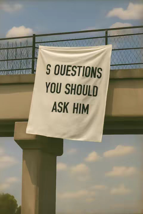 An image showing a white banner with black text hanging from a bridge support structure. The sky is blue with some clouds.