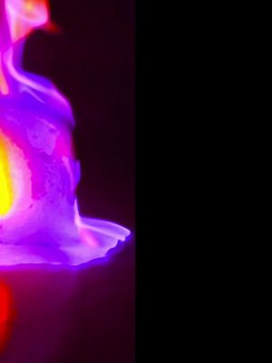 The image is vertically split into two distinct halves. The left side features a vibrant burst of colors reminiscent of a flame or energy, primarily in shades of purple, pink, yellow, and orange. These colors blend together in a dynamic, fluid pattern. The right side is completely black, providing a stark contrast to the colorful display on the left.