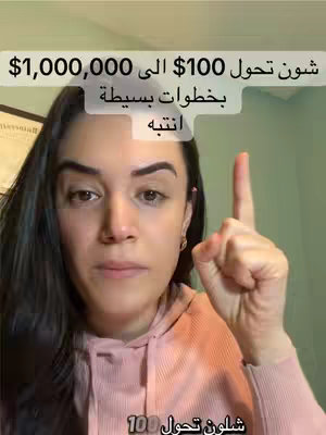 A woman with dark hair and a pink hoodie is centered in the shot with a plain background. She's pointing her index finger up, with text overlayed above her head in Arabic script. The overall composition is simple, with the focus on the woman and the message.