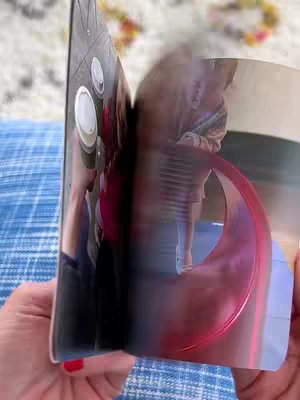 A person's hands and a book are visible. The pages of the book are being turned. The background of the image is out of focus.