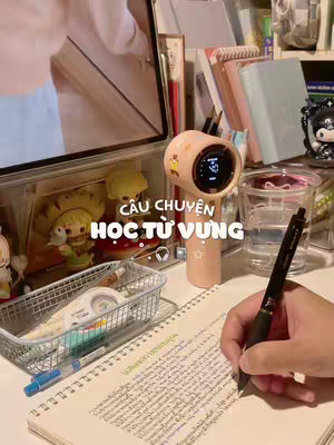 A workspace scene focused on studying Thai vocabulary. The image shows a desk with a notebook, a pen in hand, and a voice-activated recorder-speaker. The background is slightly blurred and cluttered with books and decorative items. Text in pink colors adds the hook.