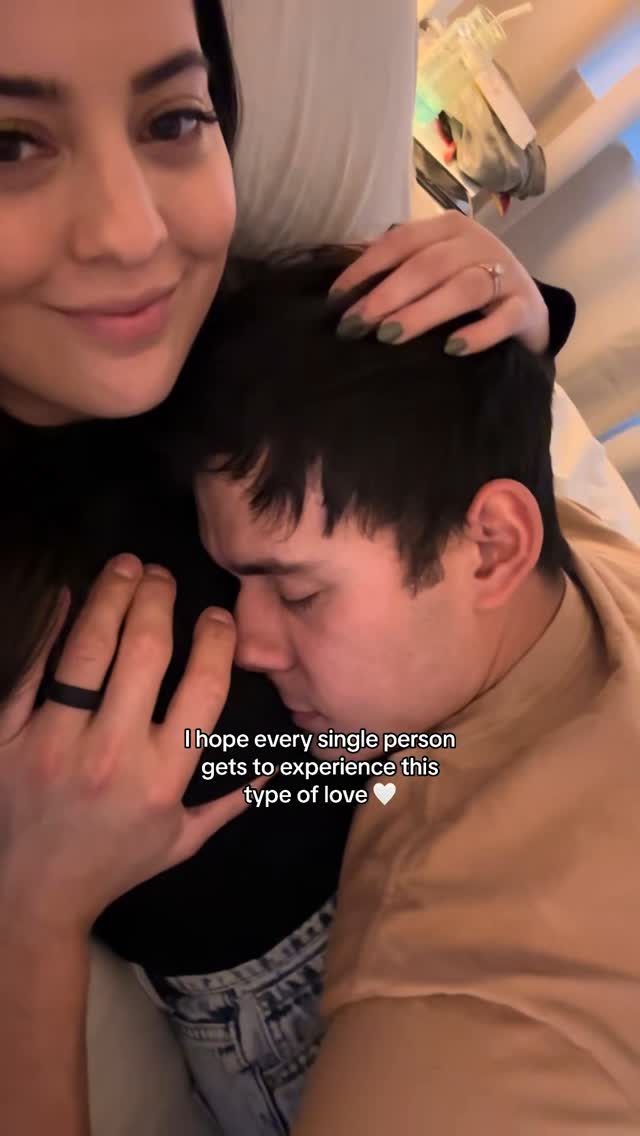 A selfie-style image of a couple embracing. A woman on the left smiles, her arm around a man in a peach-colored shirt who is leaning into her, his eyes closed. Text overlayed suggests a loving, intimate relationship.