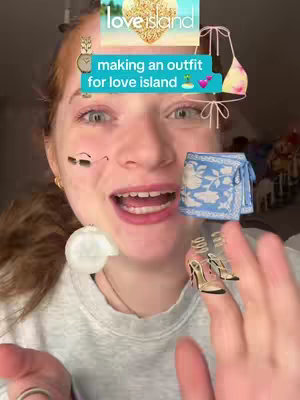 A selfie-style image shows a fair-skinned person with red hair and open eyes. They are smiling and looking at the camera. The image is overlaid with several digital illustrations of clothing items and accessories including a bikini top, a sarong, and high-heeled shoes. Text overlays say 'making an outfit' and 'for love island'. The background is blurred.