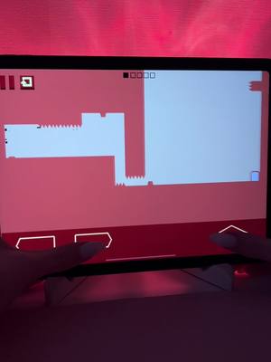 A person is playing a mobile game on an iPad. The game is a platformer with a minimalist aesthetic. The background is an even tone of red. The foreground shows the touch screen with two fingers touching the left and right side of the screen.