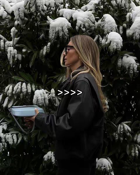 A woman in a black jacket with sunglasses stands in front of a background of snow-covered branches. The image is a side profile shot.