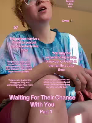 A person with blonde hair and glasses is seen from the chest up. They are wearing a tie-dye shirt, and various overlaid text boxes in pink are visible. The background appears to be a simple, light-colored wall.