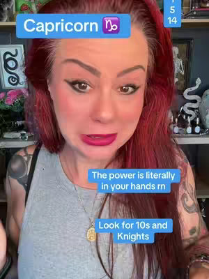 The cover image features a woman with long red hair, gazing directly at the camera with a concerned expression. She has pink lipstick and dark eyeliner. A light grey shirt is worn. Overlayed on the image are blue rectangles with white text indicating "Capricorn" with the Capricorn zodiac symbol. Other blue rectangles with text mention other factors like numbers and knights. The background is a room with decor visible on the right and some items on the left.