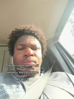 A selfie-style shot of a man inside a car. The man, who has short, dark, curly hair, is positioned in the foreground, with a slight frown. The background includes the interior of the car, with visible window and sunlight streaming in. The text overlay is in the bottom to share a bible quote.