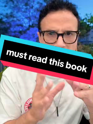 A man with glasses is in the foreground, upper body visible. He is wearing a white t-shirt and a necklace. The text "must read this book" is overlaid on the image in a diagonally oriented rectangle. The background is of out-of-focus greenery.