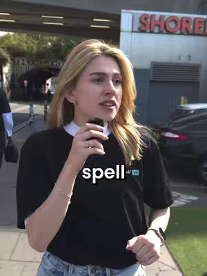 The cover image features a young woman with blonde hair, wearing a black t-shirt and jeans, standing outdoors. She is holding a microphone and appears to be speaking. The background includes a building with the word "SHORE" visible and a parked car. The overall composition is a medium shot, focusing on the woman and her immediate surroundings.
