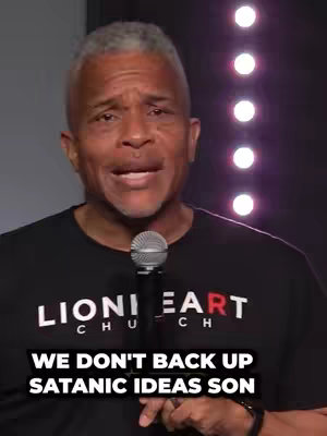 The cover image features a middle-aged man with short gray hair and a black t-shirt. He's holding a microphone and speaking passionately. Below him, overlaid in a bold, white font, is the text: WE DON'T BACK UP SATANIC IDEAS SON. The background appears to be a dim performance space with subtle, blurred lighting.