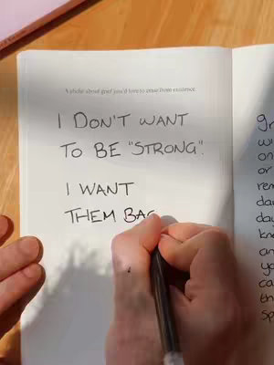 The cover image features an open book on a wooden surface. A hand holding a pen is writing on the right page. Text is handwritten in black ink, and the lighting is natural, casting shadows.