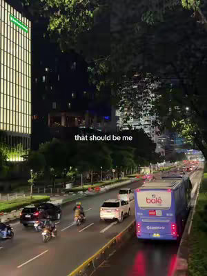 A nighttime city street scene with tall buildings illuminated on the left and a bus and traffic on the right. The hook 'that should be me' is overlaid.