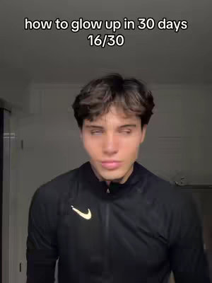 A young man with brown hair and a black jacket stands in front of a neutral background. Text overlay on the image reads 'how to glow up in 30 days 16/30'. He appears to be looking towards the side with a slightly averted gaze.