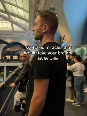 A man in a black t-shirt stands in a museum-like setting. A person in a dark jacket and white pants is on the left and other people are on the right.