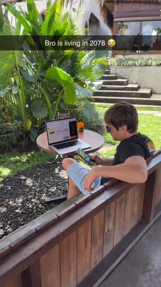 The image shows a young man sitting outside, using a laptop and a tablet. He is in a relaxed setting with greenery and a wooden bench behind him. The text overlay is near the top, in a snapchat style format.