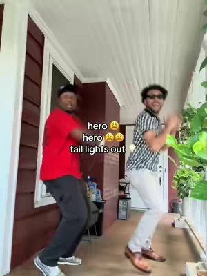 Two young men are dancing energetically on a porch. The man on the left is wearing a red shirt and black pants, and the man on the right is wearing a striped shirt and white pants. Text overlays the image.