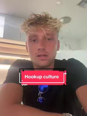A young man with blonde hair is centered in a vertically oriented video frame. He is wearing a black shirt, with the top buttons unfastened, below his neck, and has a serious expression. Text that reads "Hookup culture" on a red background and outlined in white is overlaid near the bottom of the image