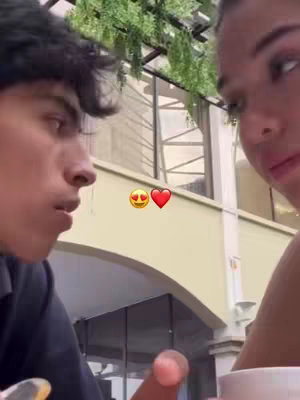 The cover image shows two people close to each other, likely in an outdoor setting. The focus is on their faces, implying intimacy, with the face of the person on the left being more clearly visible. The background consists of an architectural design with windows and greenery.