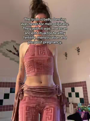 A person in a pink outfit doing a belly dance pose in a bathroom setting. Text overlay indicates the history of belly dancing.