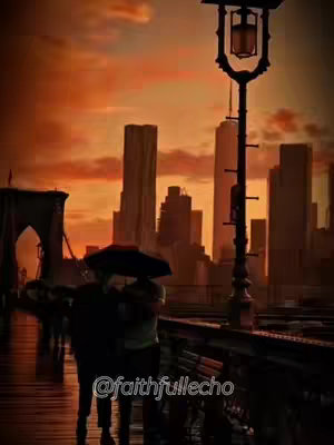 An image of a couple embracing under an umbrella on a bridge. In the background is a city skyline silhouetted against an orange and yellow sunset sky. A street lamp is positioned on the right. The image has a warm, golden color palette, reflecting the sunset lighting.