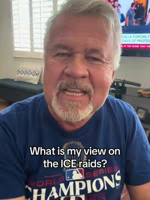 A middle-aged man with gray hair and a mustache is speaking to the camera. He is wearing a dark blue shirt with text on it and the text overlayed on the bottom reads: "What is my view on the ICE raids?"