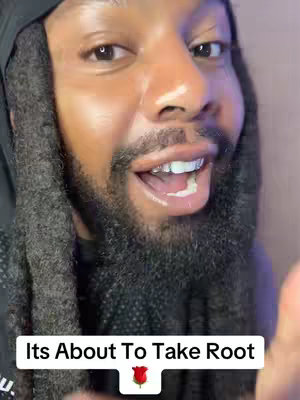 A close-up of a smiling Black man with dreadlocks, wearing a black hood and a black top looking directly at the viewer. The text overlay at the bottom says, 'Its About To Take Root' with a rose icon. The background is a gradient of soft colors.