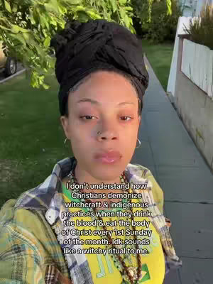 A woman with a black head wrap and hoop earrings is centered in the frame, looking towards the camera. She wears a patterned shirt and a necklace. The green foliage and a building edge are visible in the background. Text overlays the woman's image.