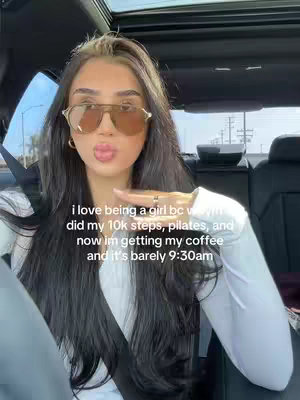 A woman sitting in the driver's seat of a car, wearing sunglasses and a white top, blows a kiss towards the camera. Text overlaid on the image describes her morning activities.
