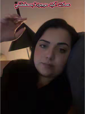 The cover image is a selfie-style video shot featuring a woman. She's positioned in the frame's center, gazing towards the camera, with a comfortable and casual setting, likely indoors, suggested by the soft lighting and the neutral background. The woman appears to be lying down or leaning against something, which positions the camera from a slightly low angle. The top of her black t-shirt is visible, and the overall composition conveys a relaxed and intimate feel.