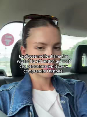 A woman is seated in a car, facing the camera. She has sunglasses perched on her head and the interior of the car is visible.