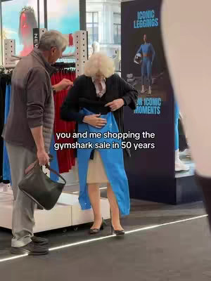 An older couple browse clothes in a Gymshark store. The woman is holding a pair of blue leggings as they are shopping. The background includes Gymshark signage.