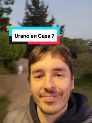 A selfie-style shot of a man in a park setting. He's in the foreground, smiling slightly at the camera. A rectangular text overlay, which is a white rectangle with text on it, appears above his head. The environment shows foliage and pathways.