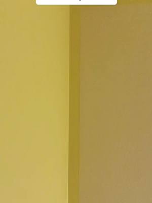 The image has a simple, minimalist composition featuring a vertical corner formed by two walls. The wall on the left is a pale yellow, while the wall on the right is a slightly darker shade of the same color, suggesting a soft, warm interior or a space with subtle lighting variations.